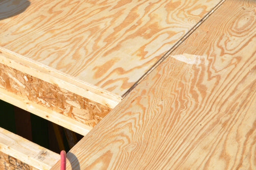 plywood subfloor before it is nailed in, sitting across the joist